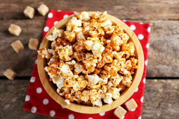 Sweet caramel popcorn in a bowl on red cotton napkin against wooden background