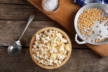 Salted popcorn in a bowl decorated with kitchen equipment on wooden table