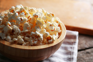 Salted popcorn in a bowl on stripped napkin with board and glass of corns on wooden table