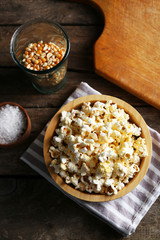 Salted popcorn in a bowl on stripped napkin with board and glass of corns on wooden table
