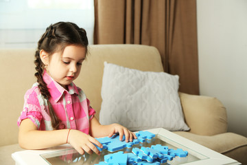 Cute little girl playing with puzzles on home interior background