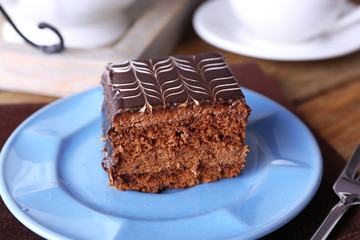 Sweet chocolate cake on blue plate with cup of tea on brown cotton serviette, close up