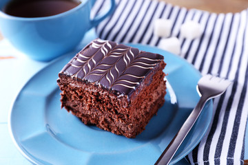 Sweet chocolate cake on blue plate with cup of tea on wooden table