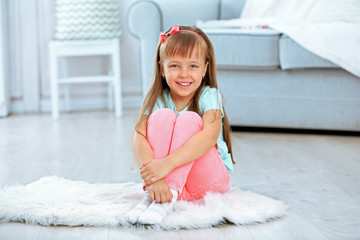 Little cute girl sitting on carpet, on home interior background