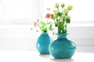 Beautiful roses in turquoise vases on window background