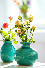 Beautiful roses in turquoise vases on window background