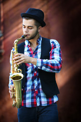 Young man playing on saxophone outside near the old wall