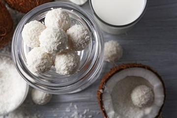 Candies in coconut flakes and fresh coconut on color wooden background