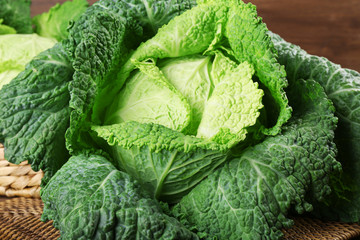 Savoy cabbage in wicker basket on wooden background, close up