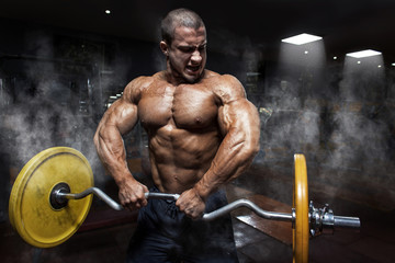 Fototapeta na wymiar Athlete muscular bodybuilder in the gym training biceps with bar