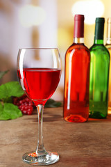 Red wine glass with colourful bottles on wooden table against unfocused background