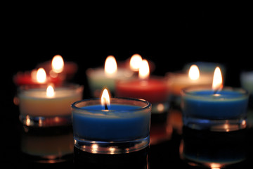 Colourful alight candles in a row on black background, blurred