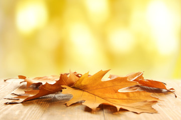 Autumn leaves on wooden table against blurred yellow background