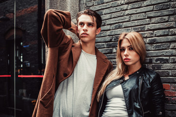 Young trendy man and woman posing in brick walls street  