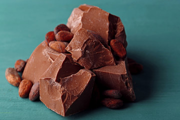 Milk chocolate pieces and cocoa beans on color wooden background