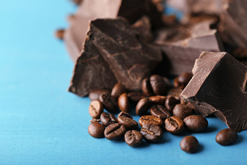 Black chocolate pieces and coffee grains on color wooden background