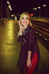 Happy stylish woman poses on the bridge at night