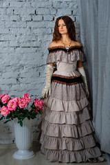 girl standing in a beautiful historic dress next to a vase of roses