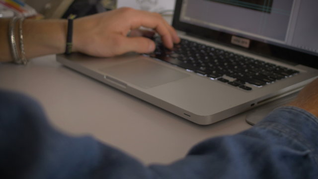 Close up of hands working then dolly and pan up to reveal the face of a young creative artist as he concentrates and uses a Wacom tablet and a laptop to create original art with brushes and pencils