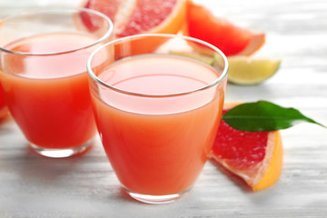 Two glasses of citrus juice and fresh fruits on light wooden background