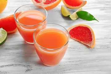 Two glasses of citrus juice and fresh fruits on light wooden background