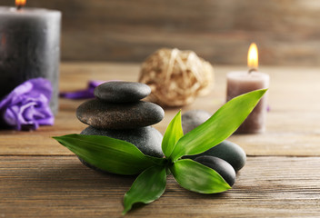 Relax set contains alight wax candles with flowers and pebbles on wooden background, focus on green leaf