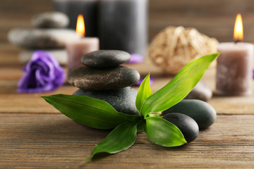 Relax set contains alight wax candles with flowers and pebbles on wooden background, focus on green leaf