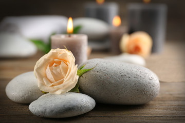 Fototapeta na wymiar Alight wax grey candles with roses and pebbles on wooden background - relax concept