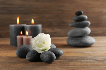Fototapeta na wymiar Alight wax grey candle with pebbles and beautiful flower on wooden background