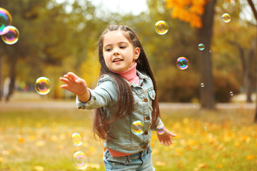 Cute girl playing with soap bubbles in park