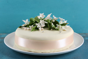 Cake with sugar paste flowers on color wooden background