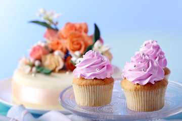 Tasty cupcakes on stand and cake, on table, on color background