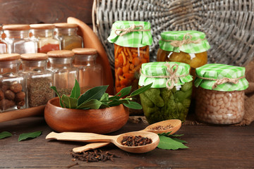 Jars with pickled vegetables, beans, spices and kitchenware on wooden background