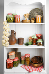 Jars with pickled vegetables and beans, spices,  kitchenware and utensils on shelf