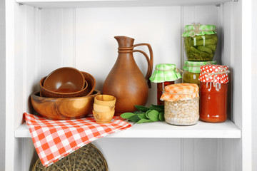 Jars with pickled vegetables and kitchenware on shelf