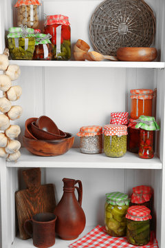 Jars with pickled vegetables and beans, spices,  kitchenware and utensils on shelf