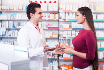 Professional pharmaceutist in drugstore helping girl