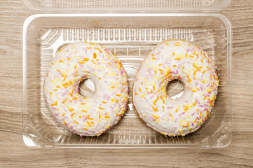 Two glazed donut with  toppings in the plastic box