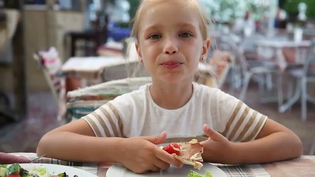 Beautiful girl eating pizza in cafe and looking at camera. Child sitting and smiling