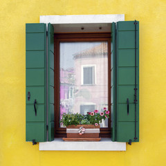 Fototapeta na wymiar Traditional colorful residential house window with opened shutters and flower pot in venetian island of Burano