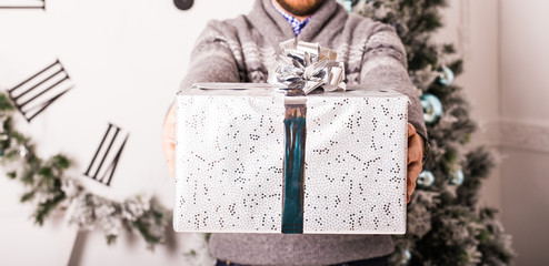 Young man holding gifts in front of Christmas tree