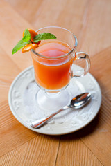 Fruit red tea with orange in glass cup, on wooden table, on bright background