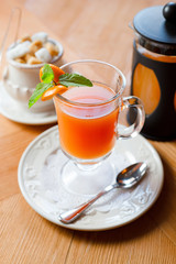 Fruit red tea with orange in glass cup, on wooden table, on bright background