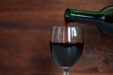 into the glass pours red wine on wooden background