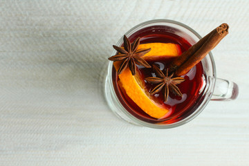 Cup with mulled wine and lemon slices and cinnamon with anise lying next to the bowl of honey on wooden table, on lights background