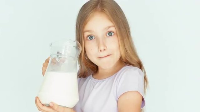 Child drinking milk from jug on a white background. Thumb up. Ok. Closeup. Milk mustache. Big eyes