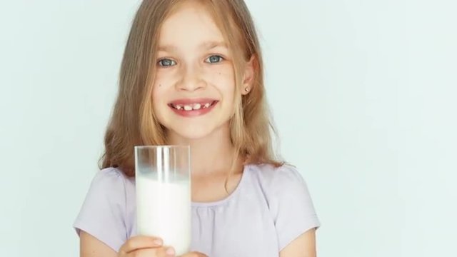 Child drinking milk. Girl showing glass of milk at camera. Girl with beautiful blond hair on a white background. Big eyes. Closeup