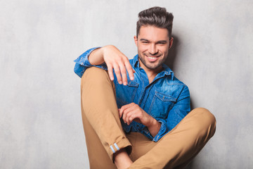 smiling man sitting in studio background legs crossed posing