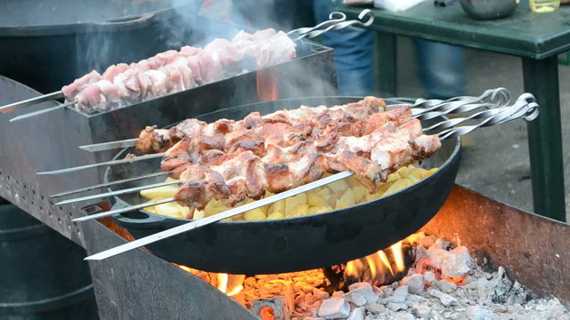 roasted smoked potatoes, small beef pieces, kebab (shashlik) on the large metal pan, street fast food in smog closeup under fire, barbecue with delicious fresh grilled meat on grill, carcinogen