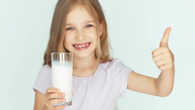 Child sniffing milk. Girl showing glass of milk at camera. Girl with beautiful blond hair on a white background. Thumb up. Ok. Closeup
